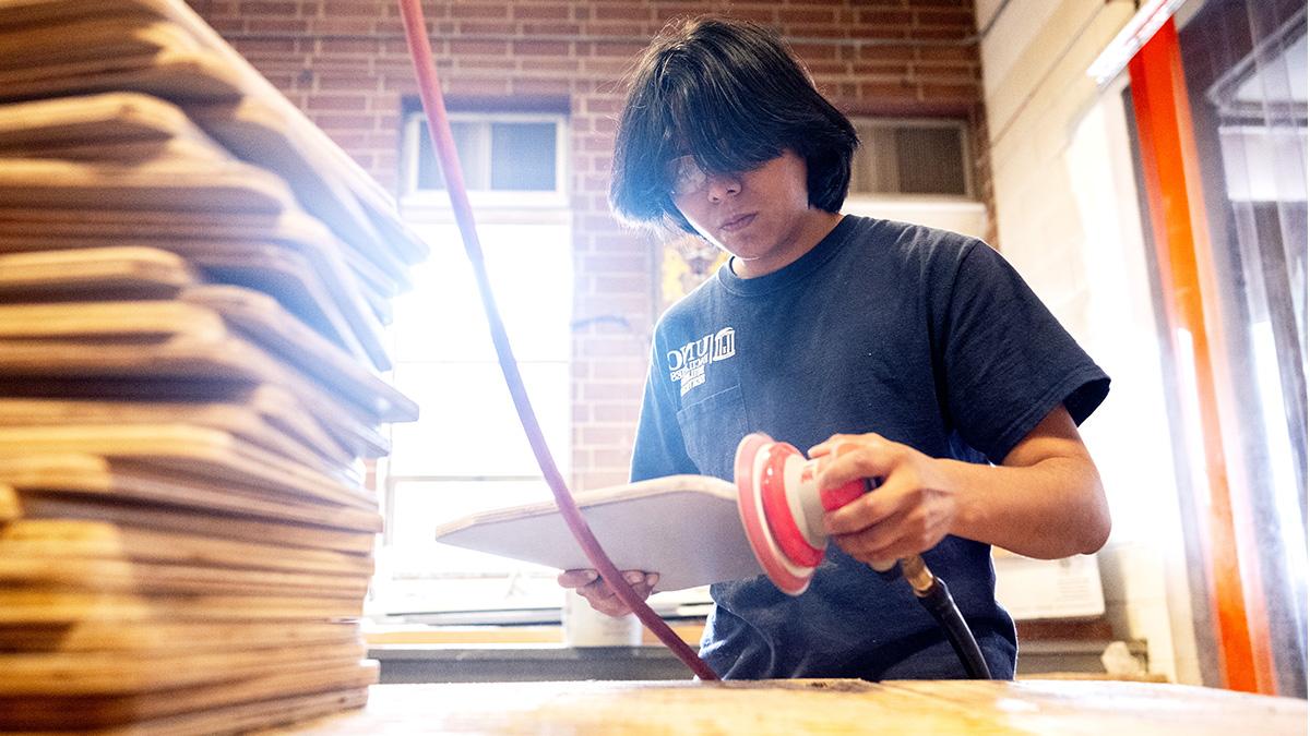 亚历克斯·埃斯科韦多戴着护目镜在博彩平台大学木工店打磨物体.